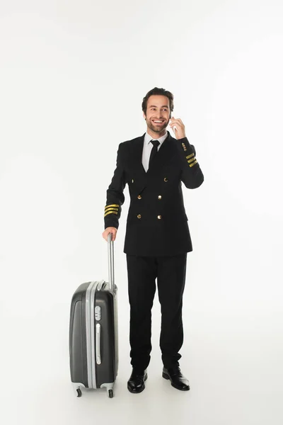 Pilote souriant parlant sur téléphone portable près de la valise sur fond blanc — Photo de stock