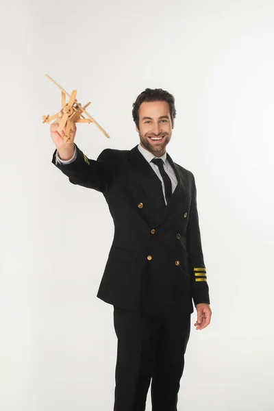 Piloto sonriente sosteniendo avión de madera aislado en blanco - foto de stock