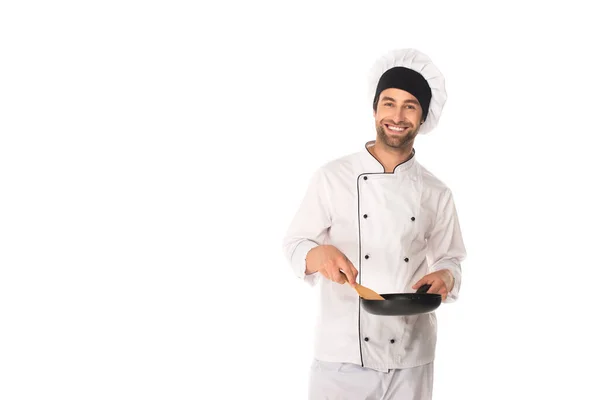 Positive chef holding frying pan and spatula isolated on white — Stock Photo