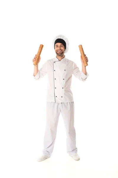 Longitud completa del chef sonriente sosteniendo molinos de pimienta y sal sobre fondo blanco - foto de stock