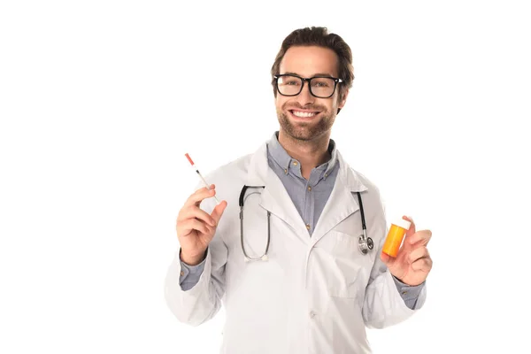 Alegre médico sosteniendo jeringa y pastillas aisladas en blanco - foto de stock