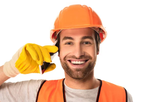 Constructor sonriente mirando a la cámara mientras habla en un teléfono inteligente aislado en blanco - foto de stock