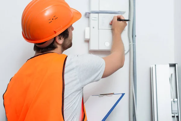 Young workman with clipboard writing on switchboard — Stock Photo
