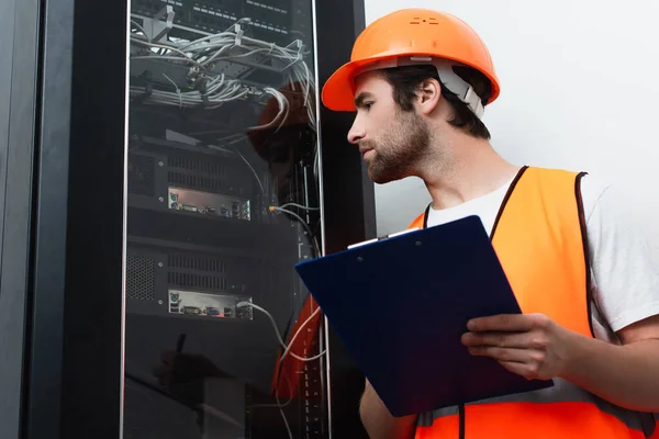 Seitenansicht des Arbeiters mit Hut, der Klemmbrett in der Nähe des Schaltschranks hält — Stockfoto