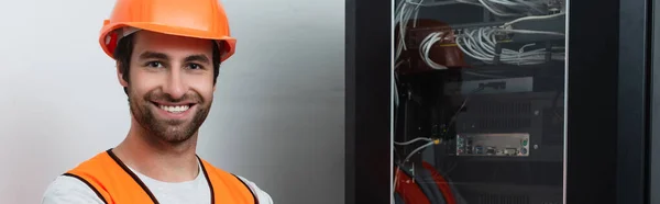 Smiling workman in hard hat looking at camera near switchboard, banner — Stock Photo