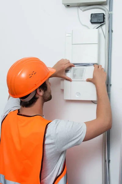 Young repairman in safety vest working with switchboard — Stock Photo