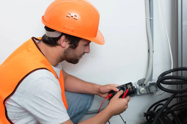 Vista lateral del trabajador sosteniendo el probador eléctrico cerca de los enchufes - foto de stock