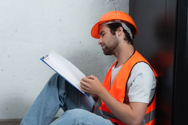 Side view of workman in hard hat looking at clipboard — Stock Photo