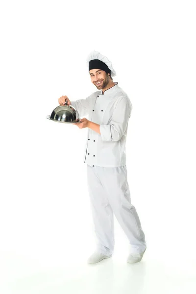 Full length of smiling chef holding cloche and tray on white background — Stock Photo