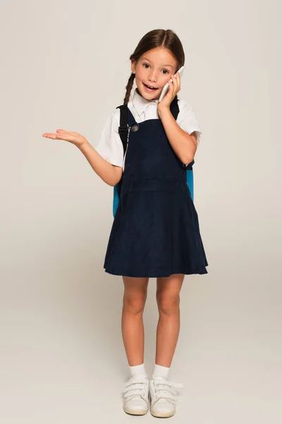 Schoolgirl talking on cellphone and pointing with hand on grey — Stock Photo