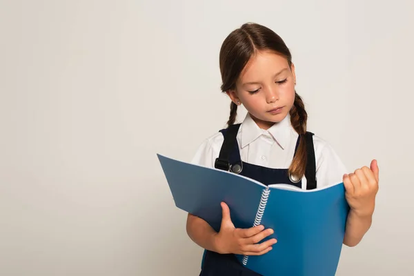 Mädchen in Schuluniform liest Notizbuch isoliert auf grau — Stockfoto