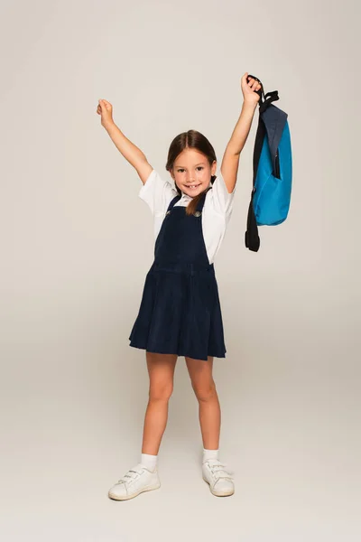 Aufgeregter Schüler mit blauem Rucksack zeigt Siegergeste auf Grau — Stockfoto