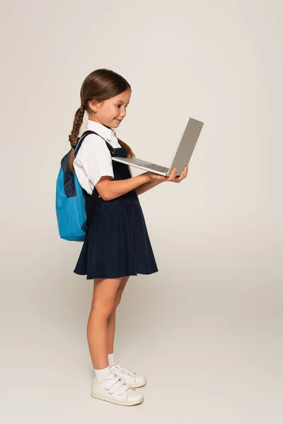 Side view of girl in school uniform using laptop on grey — Stock Photo