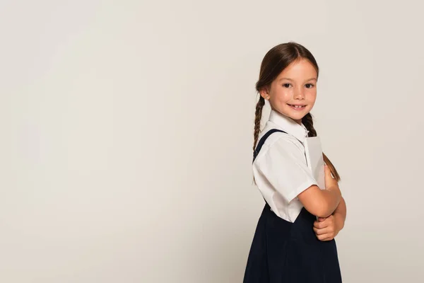 Cheerful schoolgirl with digital tablet smiling at camera isolated on grey — Stock Photo