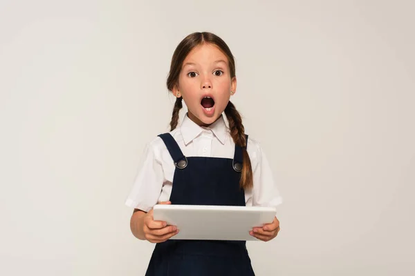 Erstaunt Schulkind mit digitalem Tablet schaut auf Kamera isoliert auf grau — Stockfoto