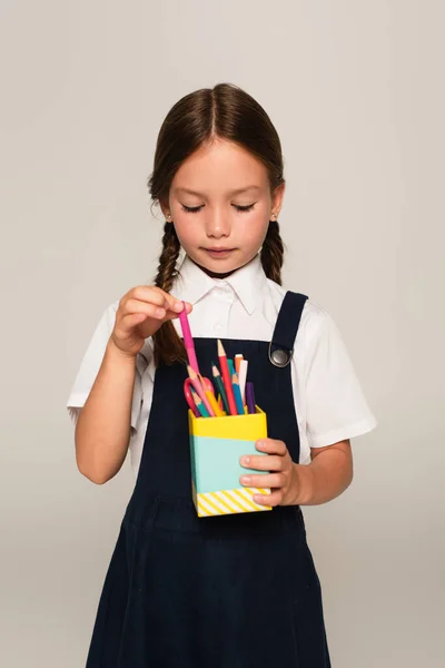 Дівчина в шкільній формі бере фетрову ручку від тримача ручки ізольовано на сірому — стокове фото