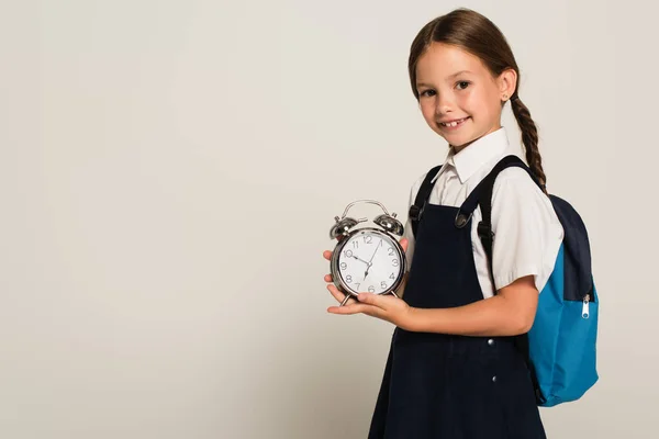 Positive schoolkid holding large alarm clock while looking at camera isolated on grey — Stock Photo