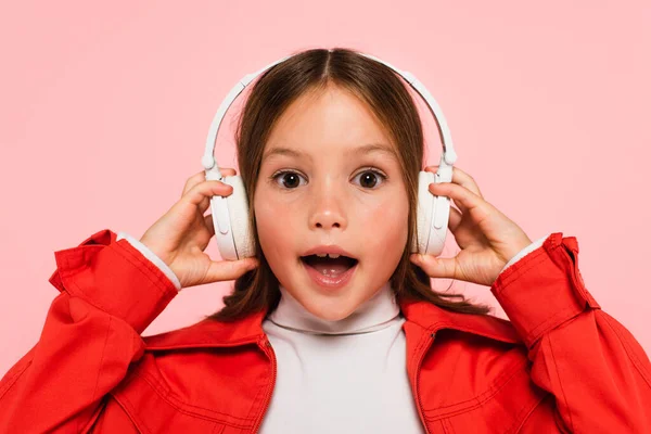 Menina espantada com boca aberta ajustando fones de ouvido isolados em rosa — Fotografia de Stock