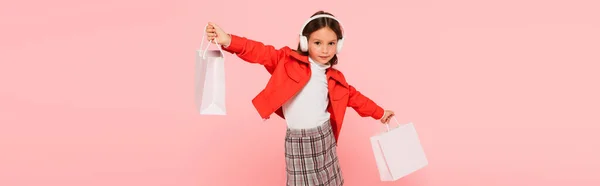 Стильна дівчина в навушниках тримає сумки для покупок ізольовані на рожевому, банер — стокове фото