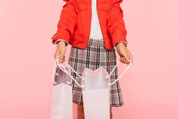 Vista recortada de niño en chaqueta naranja y falda a cuadros abriendo bolsa aislada en rosa - foto de stock