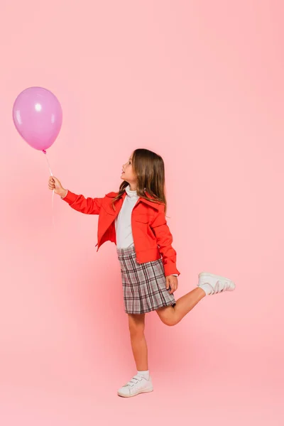 Girl in orange jacket and plaid skirt holding festive balloon on pink — Stock Photo