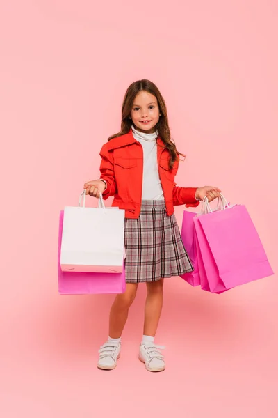 Дівчина в плетеній спідниці та апельсиновій куртці тримає сумки на рожевому — стокове фото