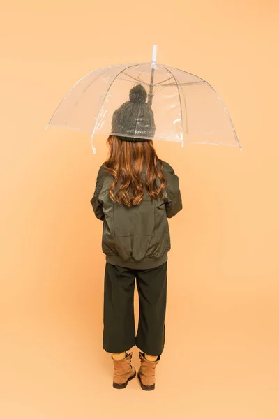 Back view of trendy girl standing under transparent umbrella on beige — Stock Photo