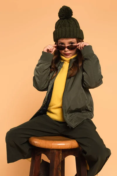 Niño en traje de otoño de moda mirando a la cámara sobre gafas de sol con estilo aislado en beige - foto de stock