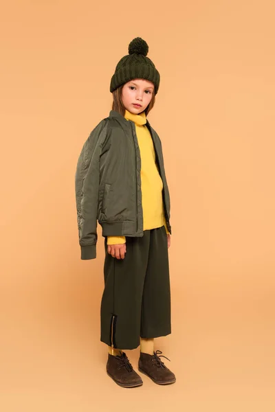 Full length view of child with jacket on shoulders looking at camera on beige — Stock Photo