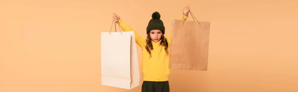 Criança na moda em gola alta amarela segurando sacos de compras em mãos levantadas isolado em bege, banner — Fotografia de Stock