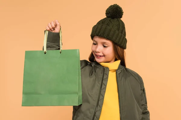 Smiling girl in jacket and brown hat holding shopping bag isolated on beige — Stock Photo