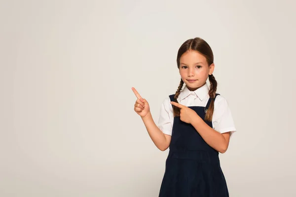 Girl in school uniform pointing with fingers isolated on grey — Stock Photo