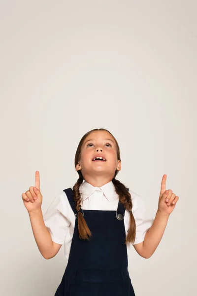 Überraschtes Schulkind blickt auf und zeigt mit erhobenen Fingern auf grau — Stockfoto