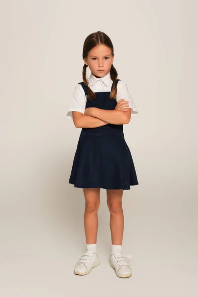 Full length view of offended schoolchild standing with crossed arms on grey — Stock Photo