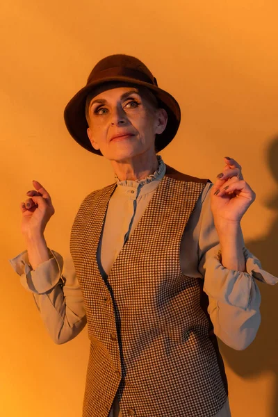 Mulher idosa em roupas vintage em pé sobre fundo laranja — Stock Photo