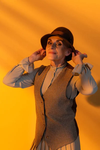 Mujer anciana con estilo en sombrero vintage sobre fondo naranja — Stock Photo