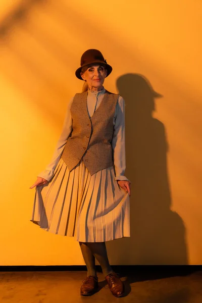 Longitud completa de la mujer mayor en sombrero que sostiene la falda sobre fondo naranja — Stock Photo