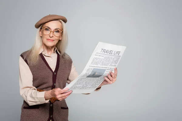 Ältere Frau mit Brille hält Reisezeitung isoliert auf Grau — Stockfoto