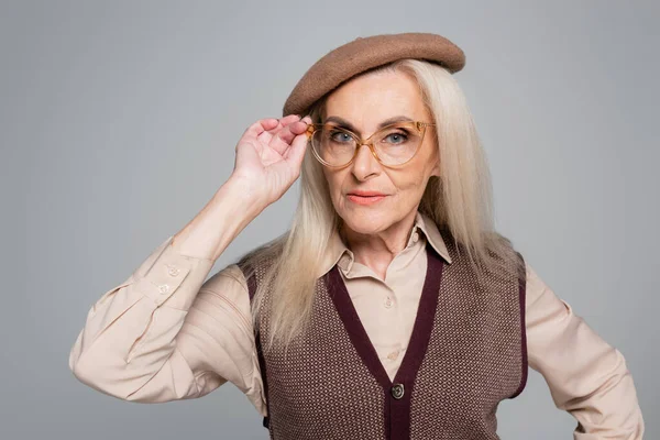 Модна старша жінка в береті тримає окуляри ізольовані на сірому — стокове фото