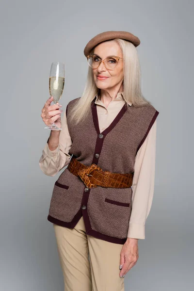 Seniorin mit Brille hält Glas Champagner isoliert auf Grau — Stockfoto