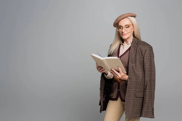 Fashionable woman in jacket and beret reading book isolated on grey — Stock Photo