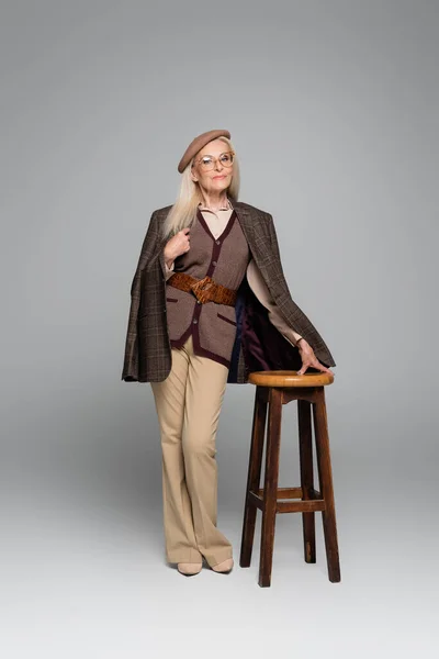 Stilvolles Senior-Model posiert in der Nähe von Stuhl auf grauem Hintergrund — Stockfoto