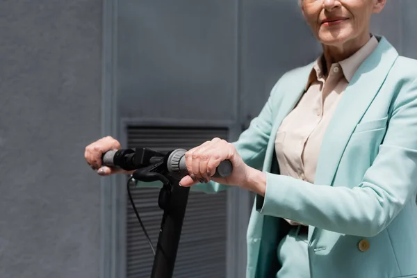 Cropped view of senior businesswoman standing near eclectic kick scooter outdoors — Stock Photo