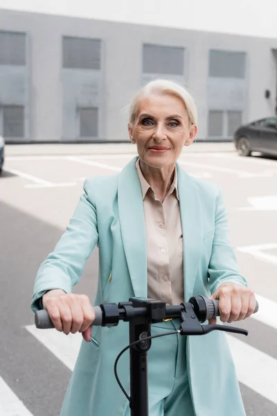 Empresária sênior olhando para a câmera perto de scooter de chute elétrico — Fotografia de Stock