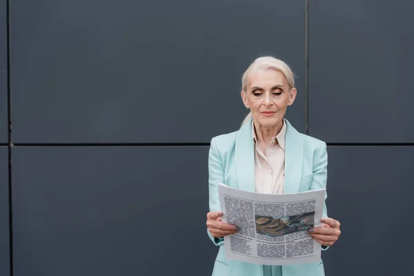 Старшая деловая женщина читает газету возле здания на открытом воздухе — стоковое фото