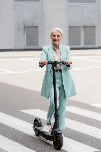 Alegre mujer de negocios senior de pie cerca de scooter de patada eléctrica - foto de stock