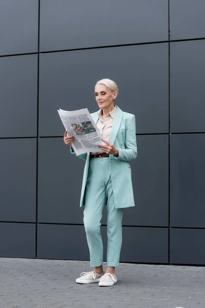 Старшая деловая женщина читает газету, стоя возле здания — стоковое фото