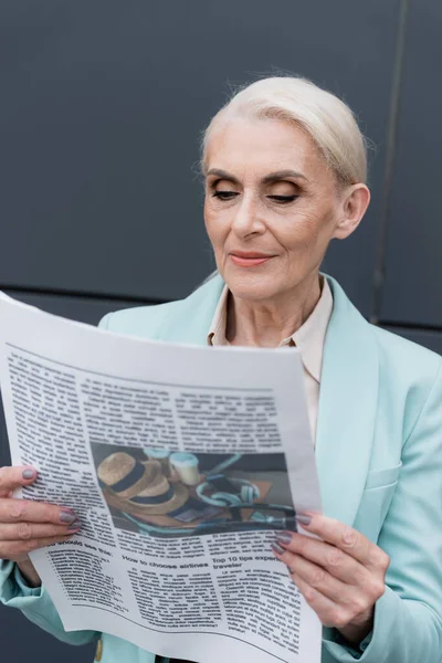 Donna d'affari anziana che legge giornali offuscati all'aperto — Foto stock
