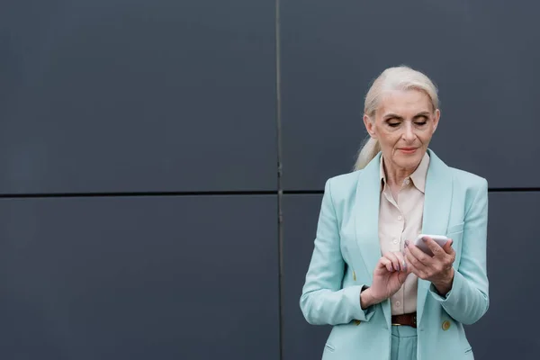 Ältere Geschäftsfrau nutzt Smartphone in der Nähe von Gebäuden — Stockfoto