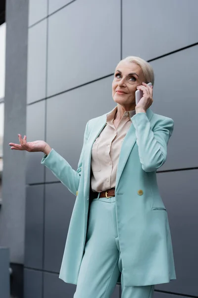 Seniorin in Dienstkleidung spricht auf Smartphone in der Nähe von Haus im Freien — Stockfoto